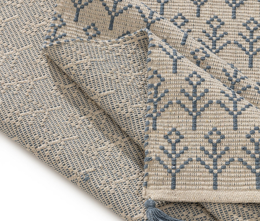 Nahaufnahme eines beigen Teppichs mit blauem Baummuster und einer blauen Quaste.