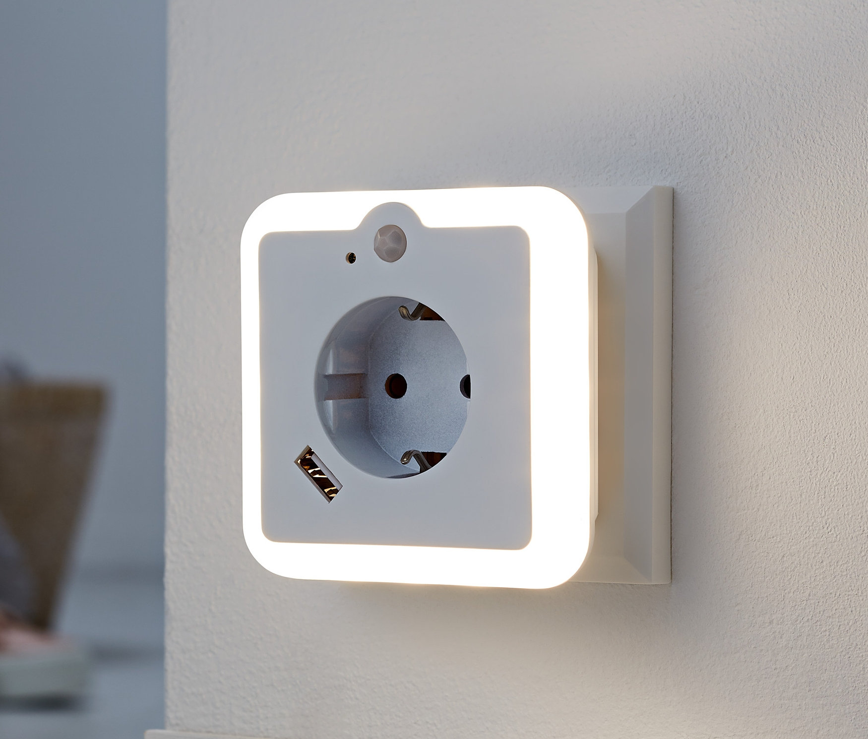 An einer weißen Wand ist ein LED-Nachtlicht mit Steckdose und USB-Lademöglichkeit.