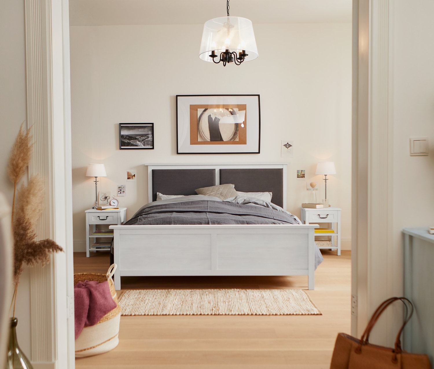 Schlafzimmer mit Bett mit gepolstertem Kopfteil, ca. 160 x 200 cm, Nachttisch mit Schublade und Tischleuchte mit Textilschirm.