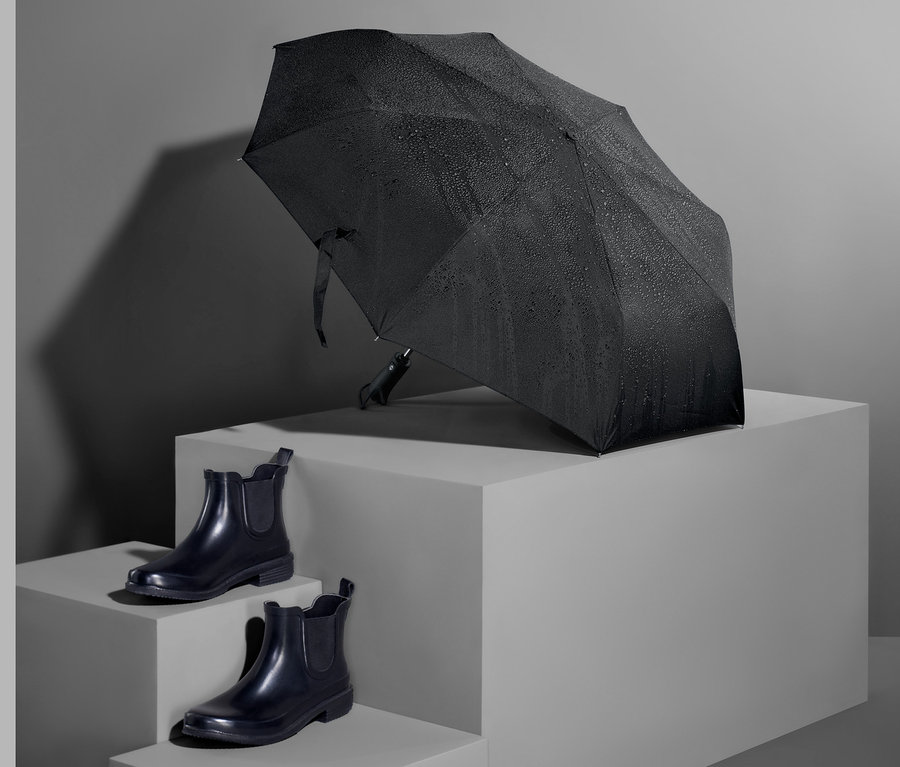 Ein schwarzer Automatik-Taschenschirm und ein Paar schwarze Schuhe auf grauem Hintergrund.