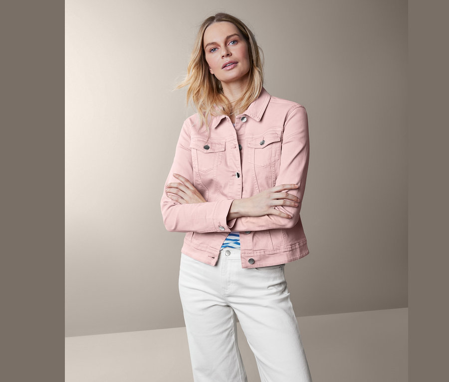 Frau posiert in roséfarbener Jeansjacke und weißen Hosen.