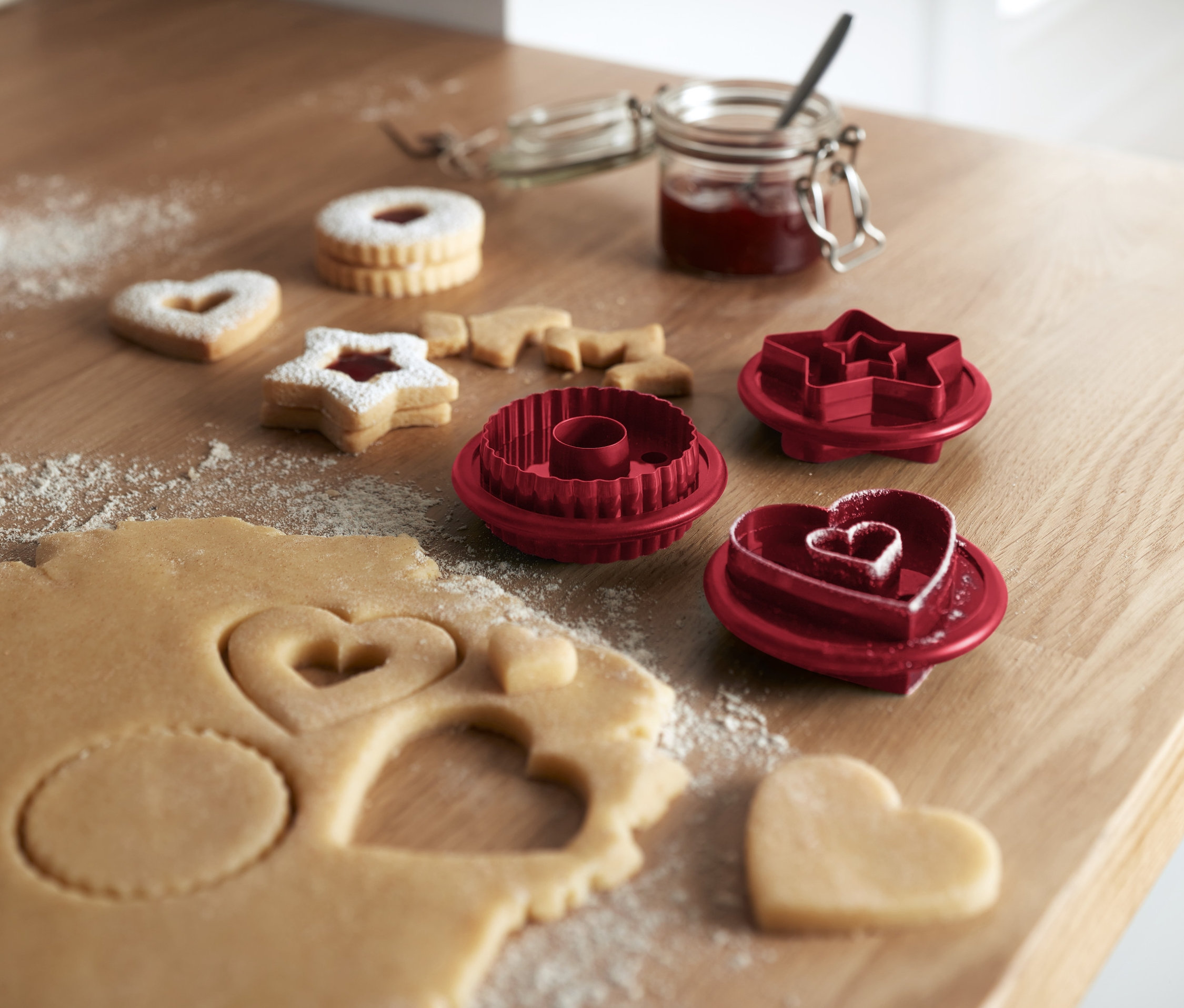 Teig mit 3 Linzer Plätzchenausstechern und gebackene Kekse auf einem Holztisch.