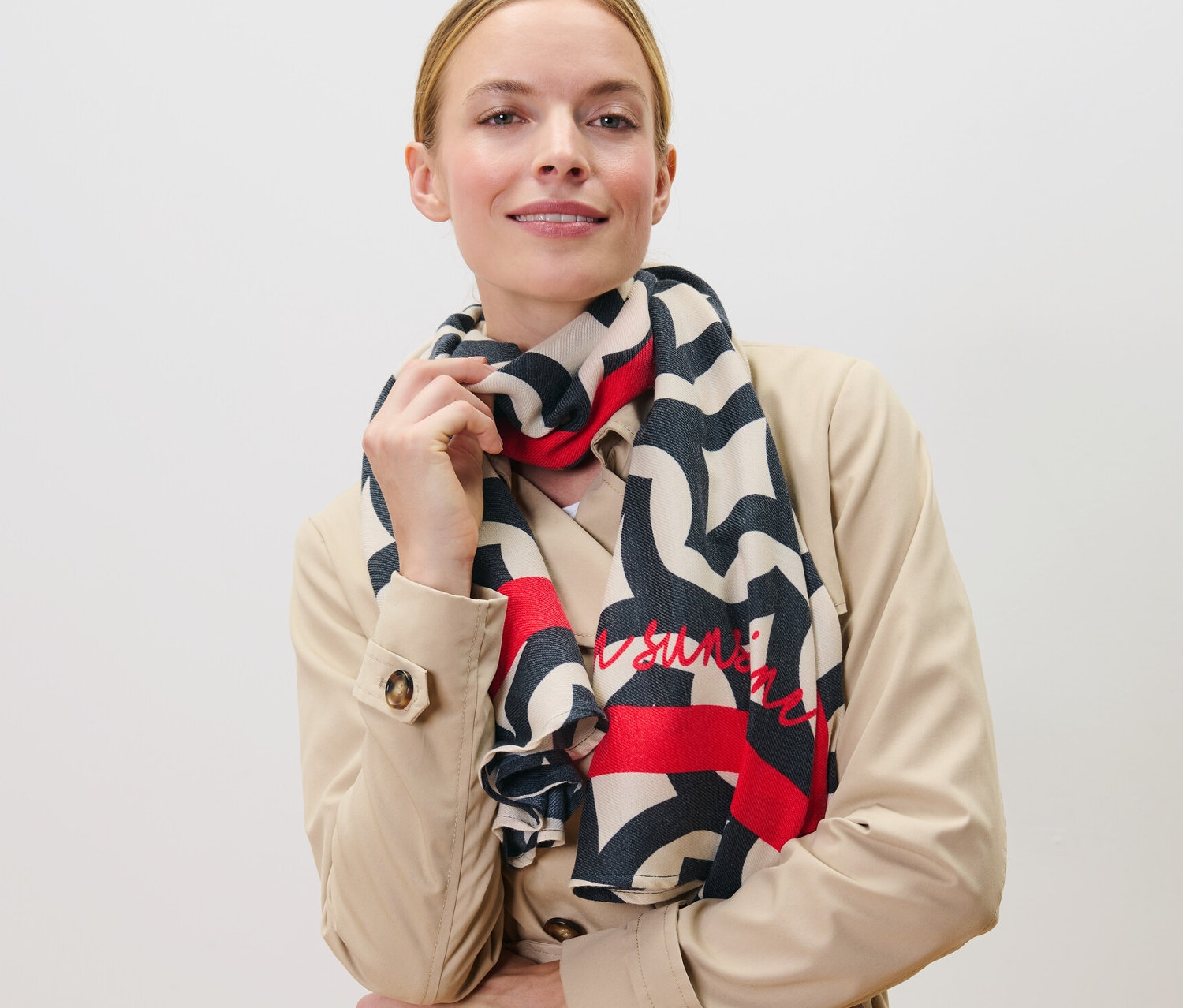 Frau posiert in beigem Trenchcoat mit bedrucktem Webschal.
