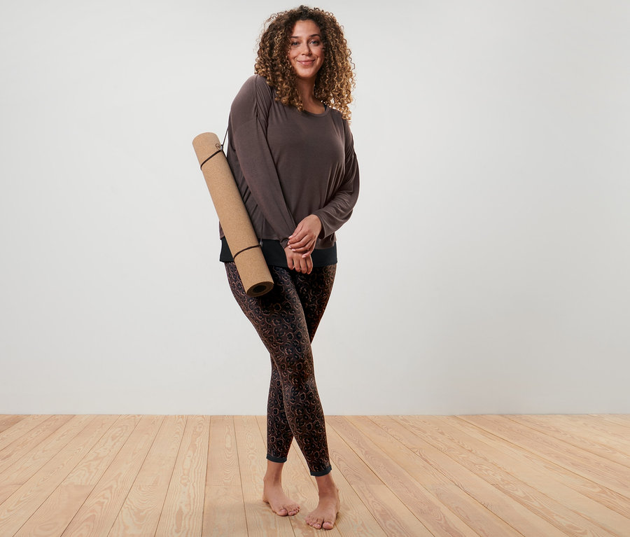 Frau posiert mit einem braunen 2-in-1-Sportshirt und einer schwarzen und braunen Wende-Sporttight.