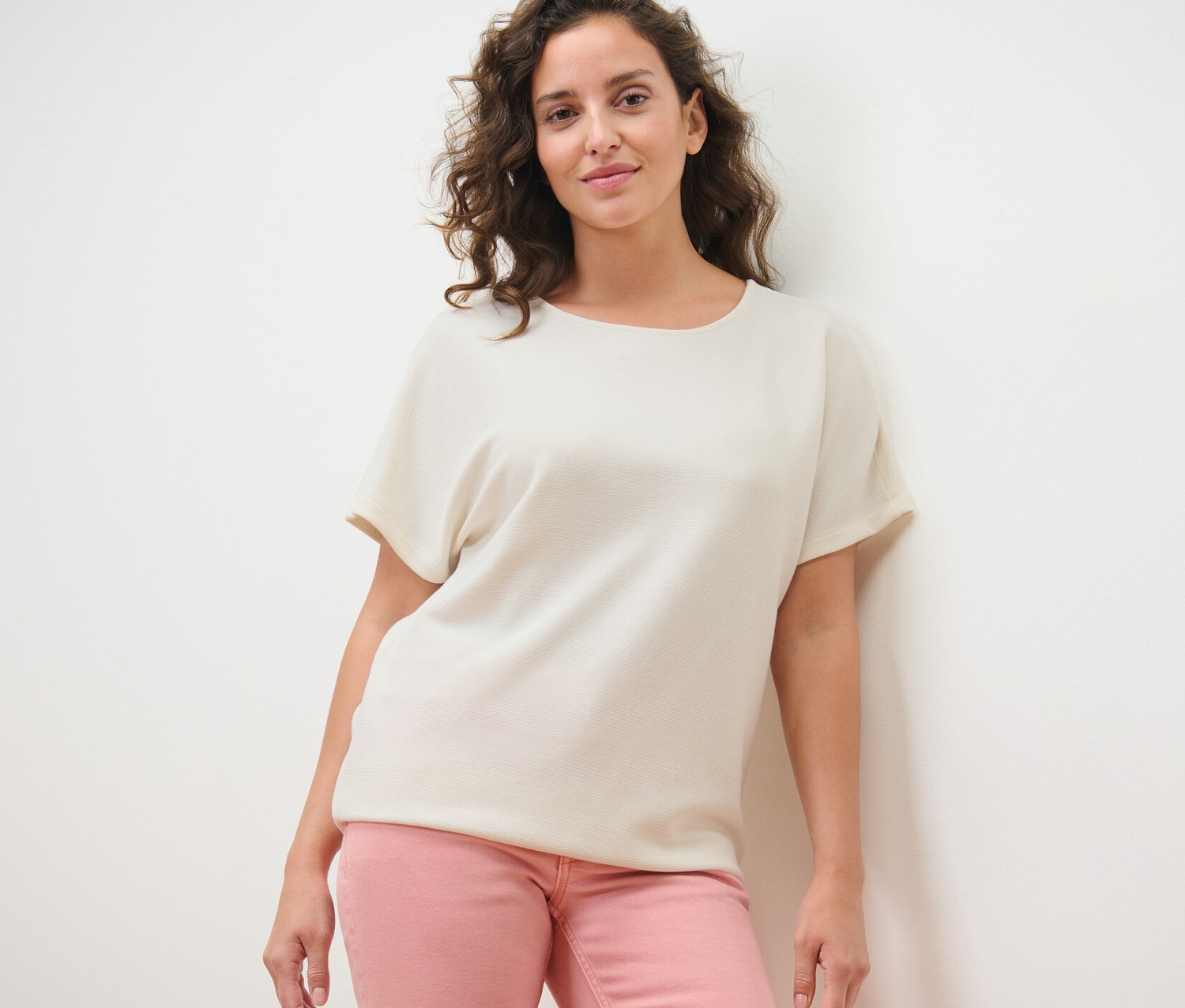 Frau posiert in einem cremeweißen Blusenshirt und einer rosafarbenen Hose.