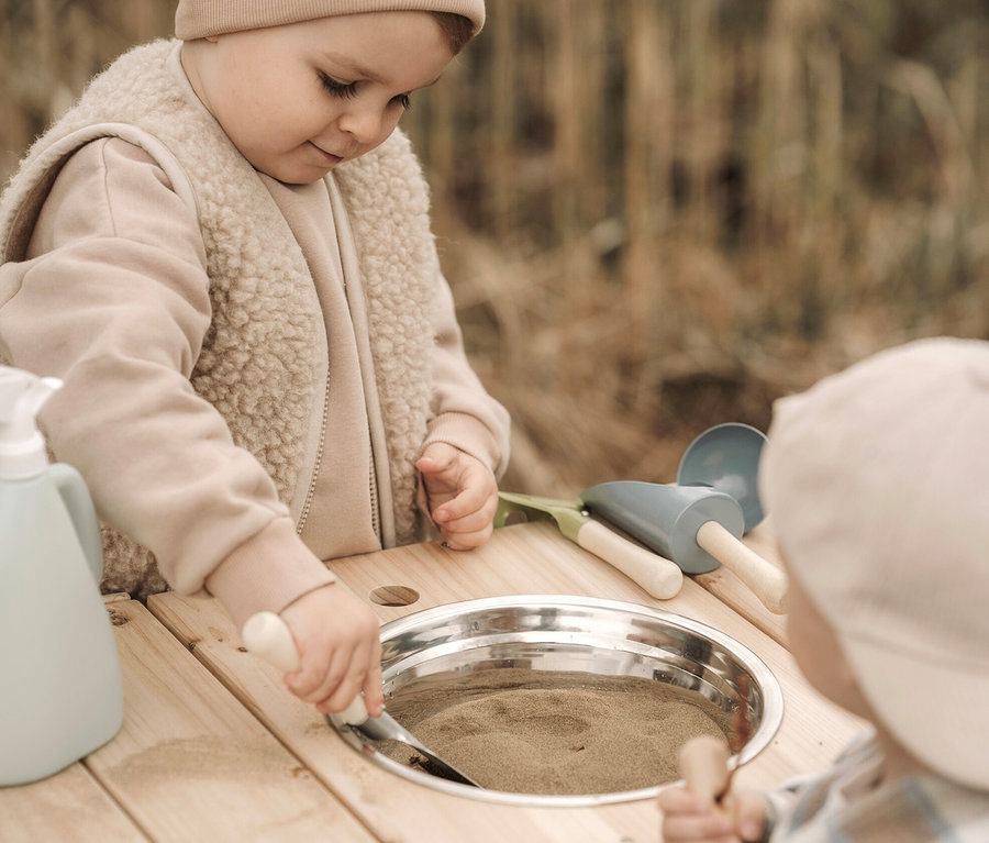 Zwei Kinder spielen mit einer small foot Matschküche kompakt und einem small foot Gartenwerkzeug-Set, groß.