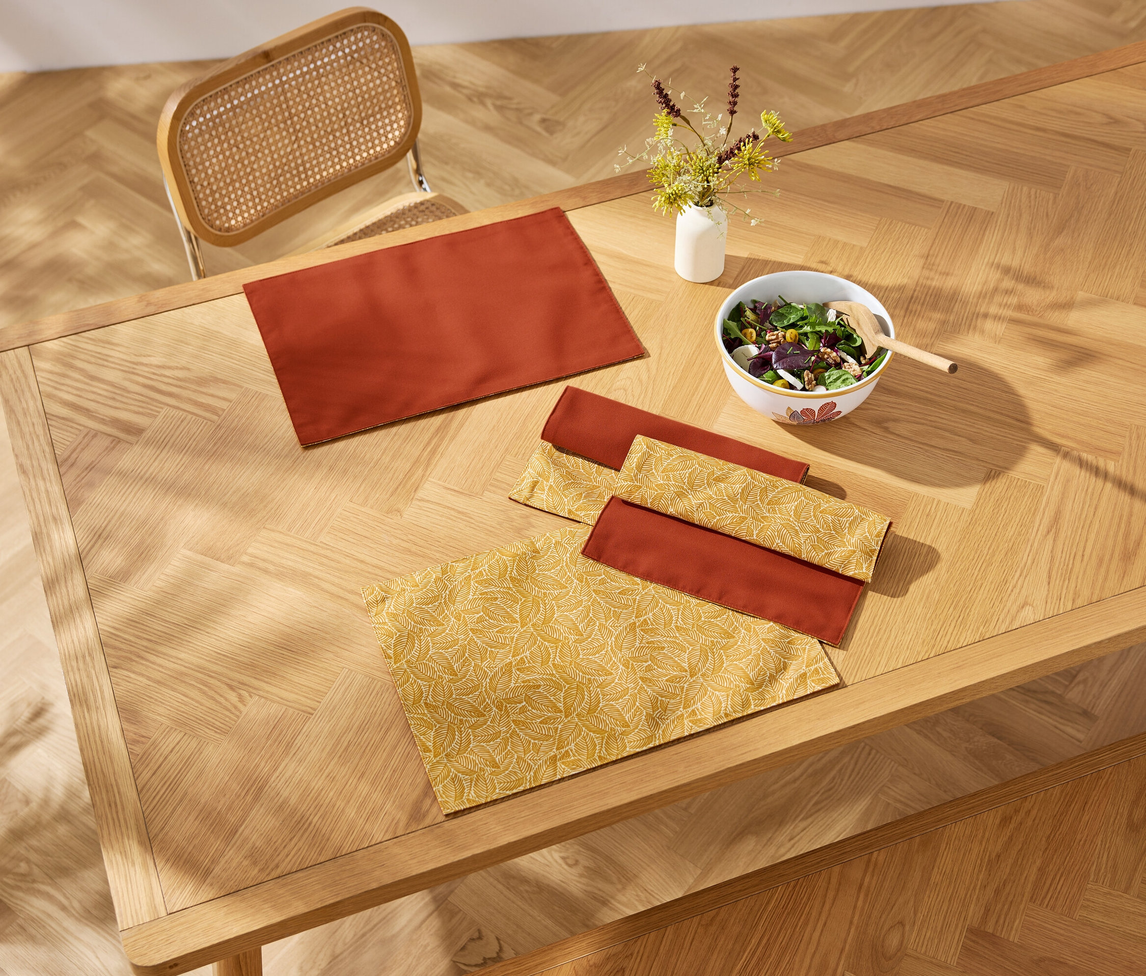 Draufsicht auf einen Holztisch mit Tischsets, Servietten und einer Schüssel Salat.