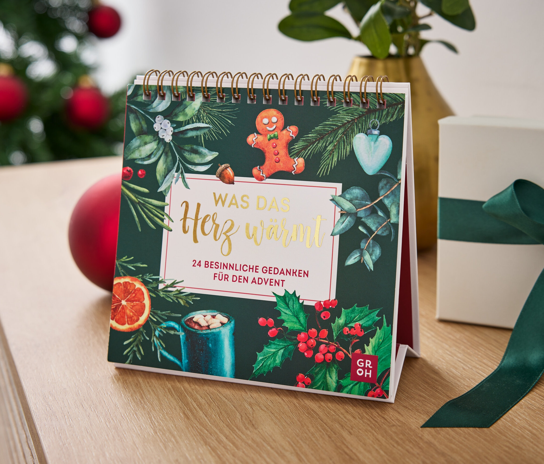 Tischkalender mit Weihnachtsmotiv und Geschenkbox mit grünem Band auf einem Tisch.