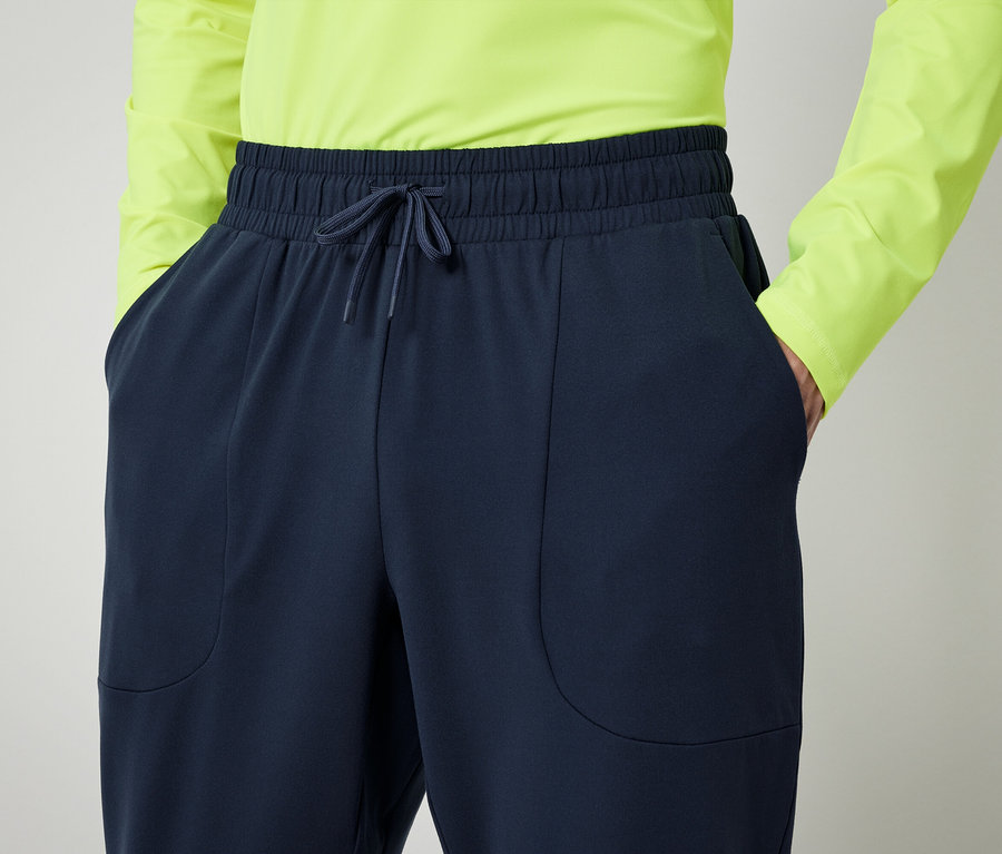 Person im neongrünem Hemd und marineblauer Hose mit Händen in den Taschen.