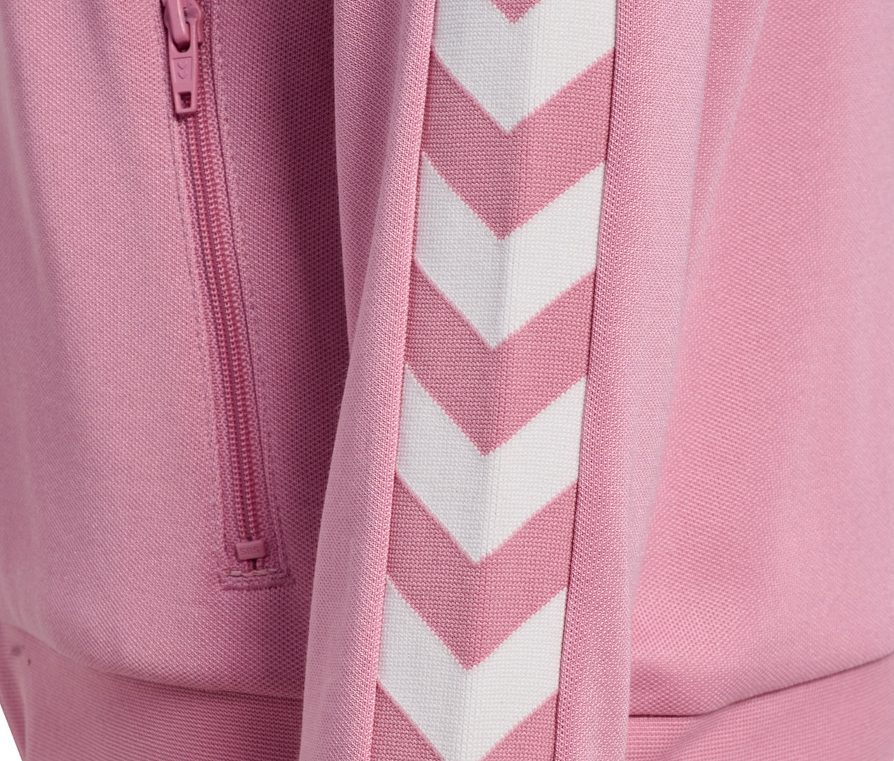 Detailansicht einer rosa Hummel HMLJR Archive Reg Poly Zip Jacket mit weißen Chevron-Streifen und Reißverschlusstasche.