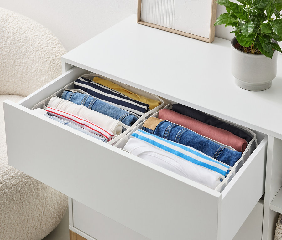 Eine offene Schublade einer weißen Kommode enthält ordentlich gefaltete Kleidung in Aufbewahrungsboxen.