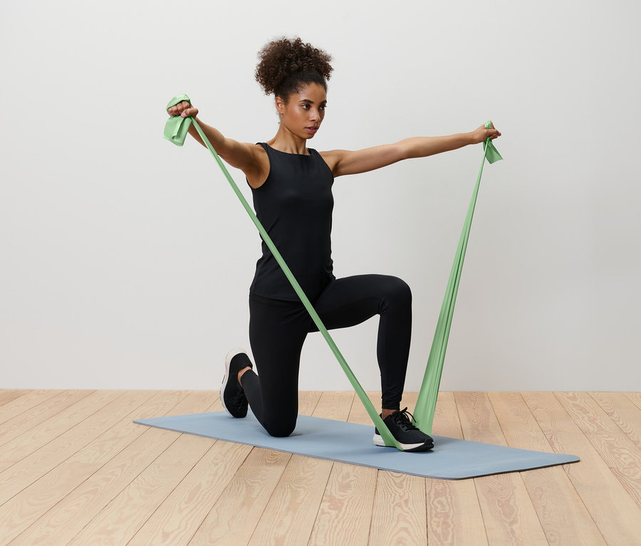 Eine Frau kniet auf einer blauen Yogamatte und dehnt ein grünes Widerstandsband.