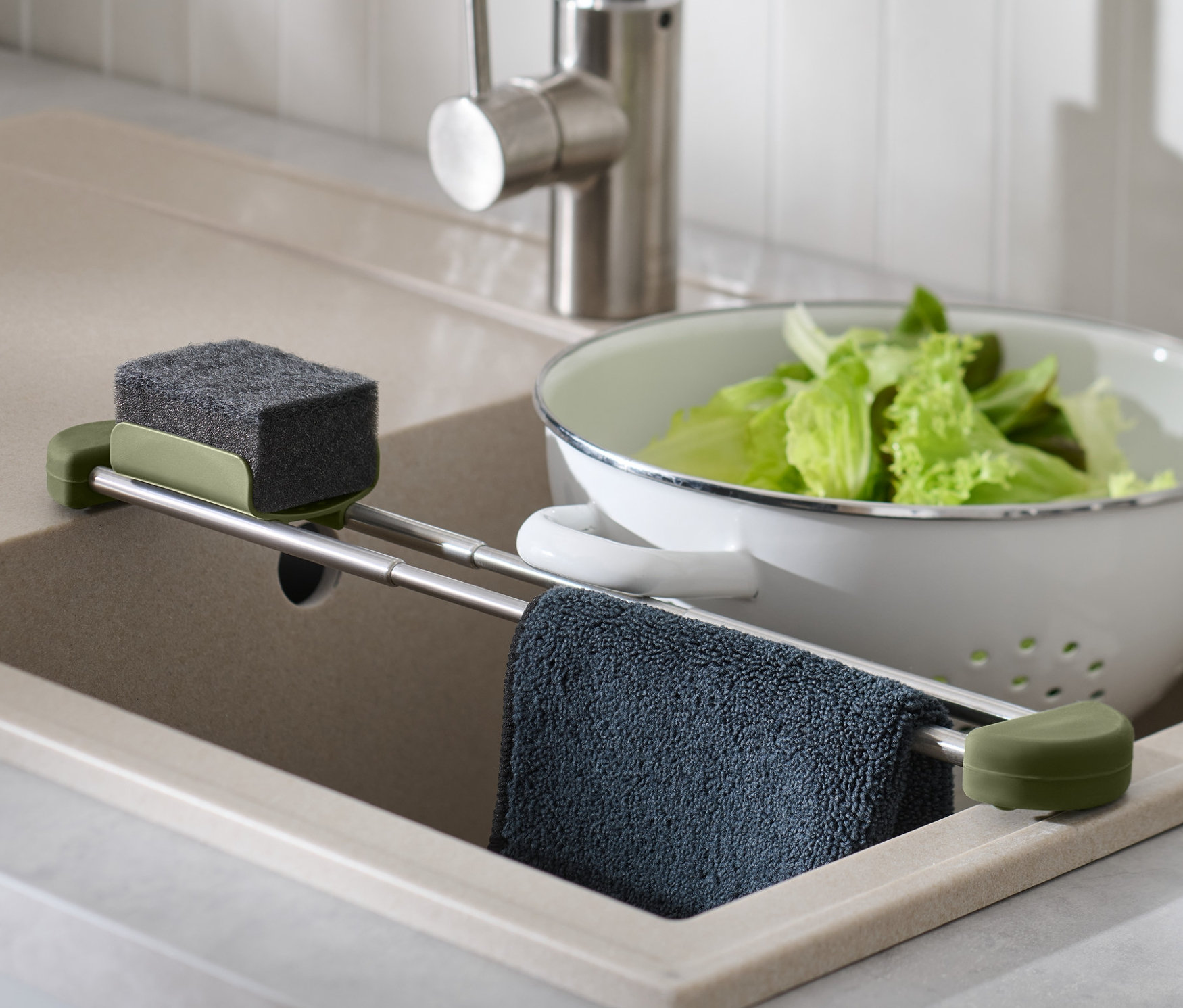 Im Spülbecken befindet sich ein ausziehbarer Spülbecken-Organizer mit Schwamm, Lappen und Salat in einem Durchschlag.