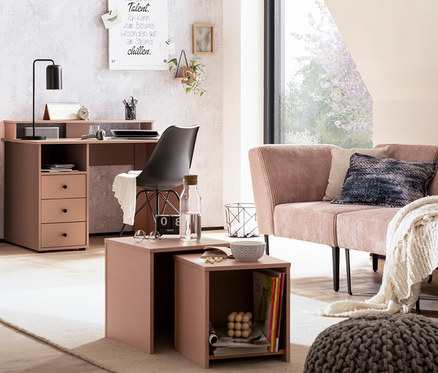 Ein Zimmer mit einem beigen Sofa, einer Korbleuchte und apricotfarbenen Smash-Möbeln, darunter eine Kommode, ein Nachttisch und ein Schreibtisch.