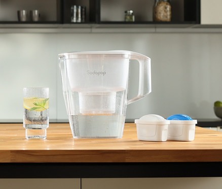 Auf einer Küchentheke stehen ein Sodapop Wasserfilter »Selina« inklusive Kartuschen und ein Glas Wasser.