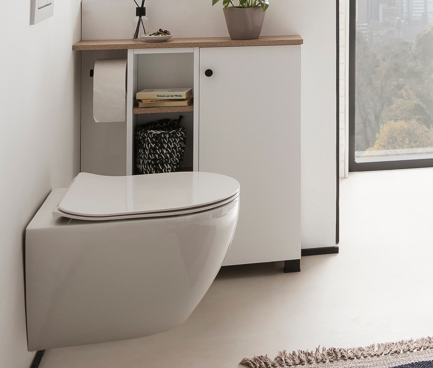 Hänge-WC neben weißem, mattem Badschrank Balto mit Holzplatte und offenem Regal.