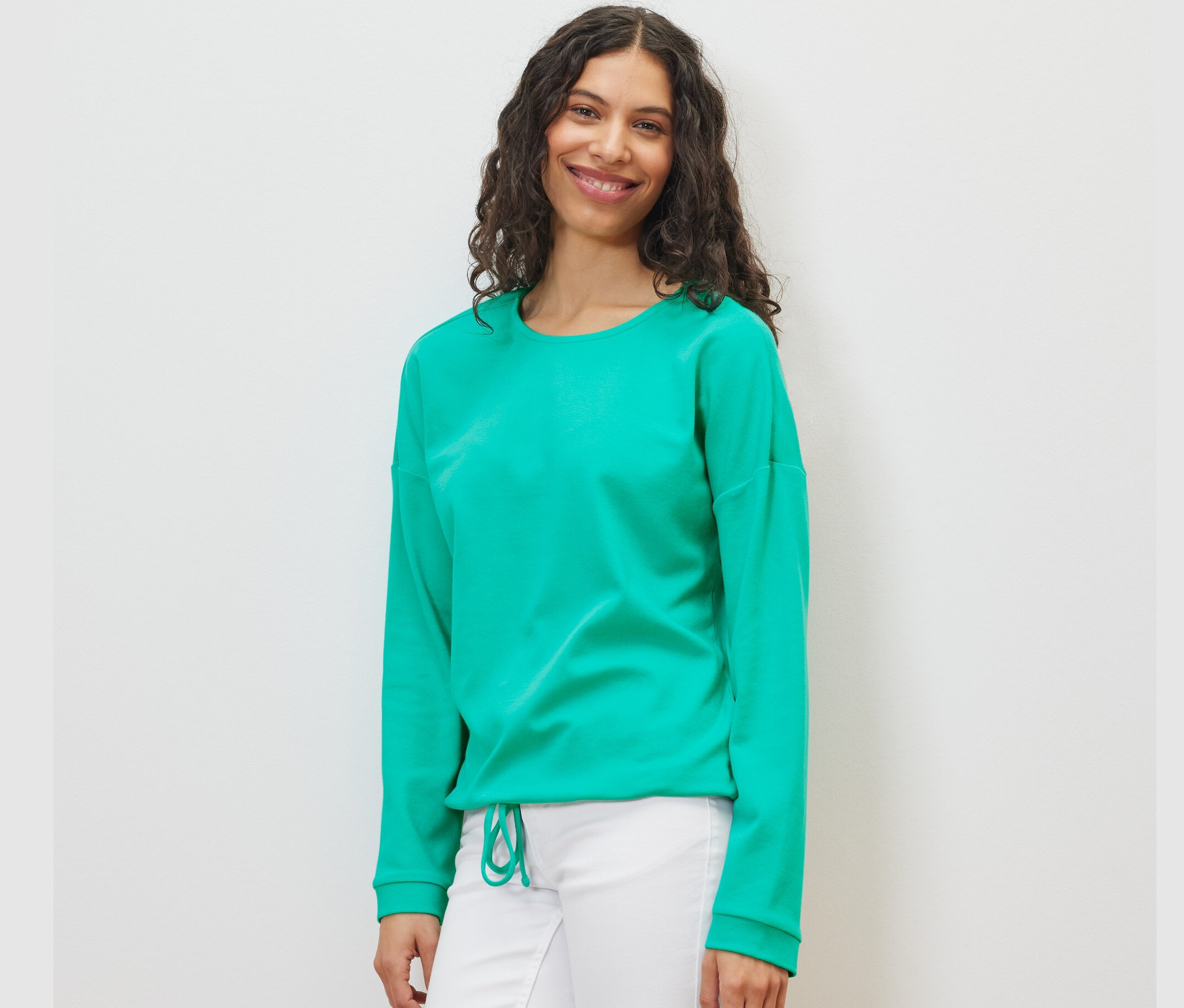 Frau trägt ein Sweatshirt in Aqua und eine weiße Hose.