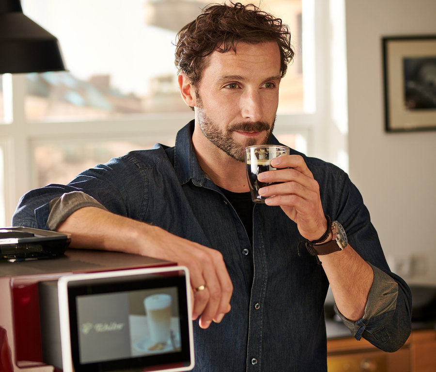 Mann trinkt Kaffee, lehnt an rotem »Tchibo Office« Kaffeevollautomat.