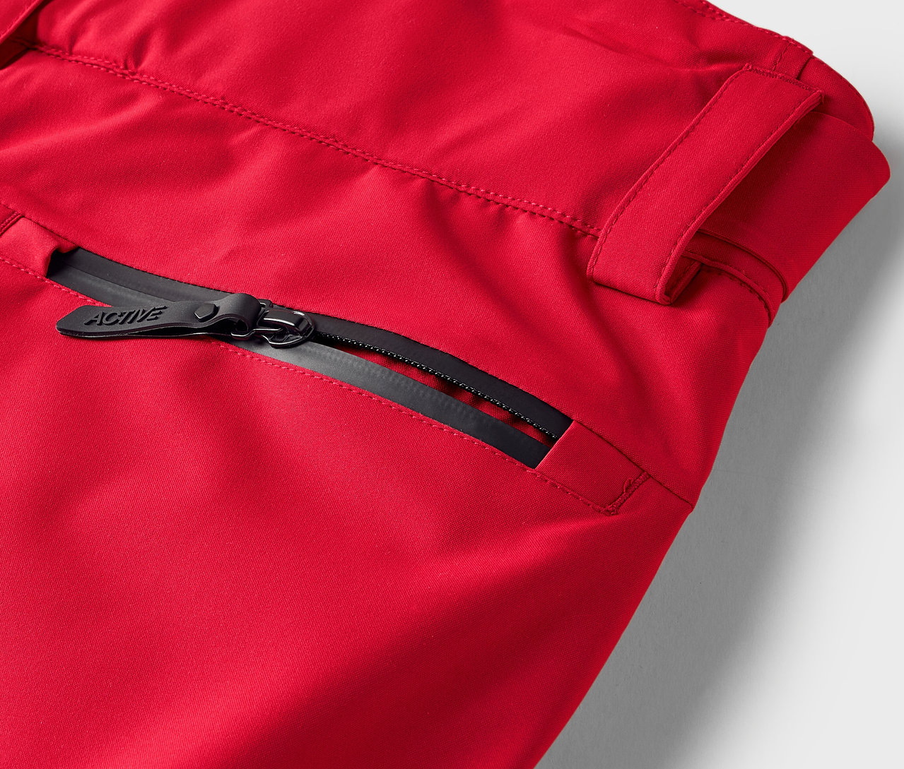 Detail einer roten Hose mit schwarzem Reißverschluss an der Tasche.