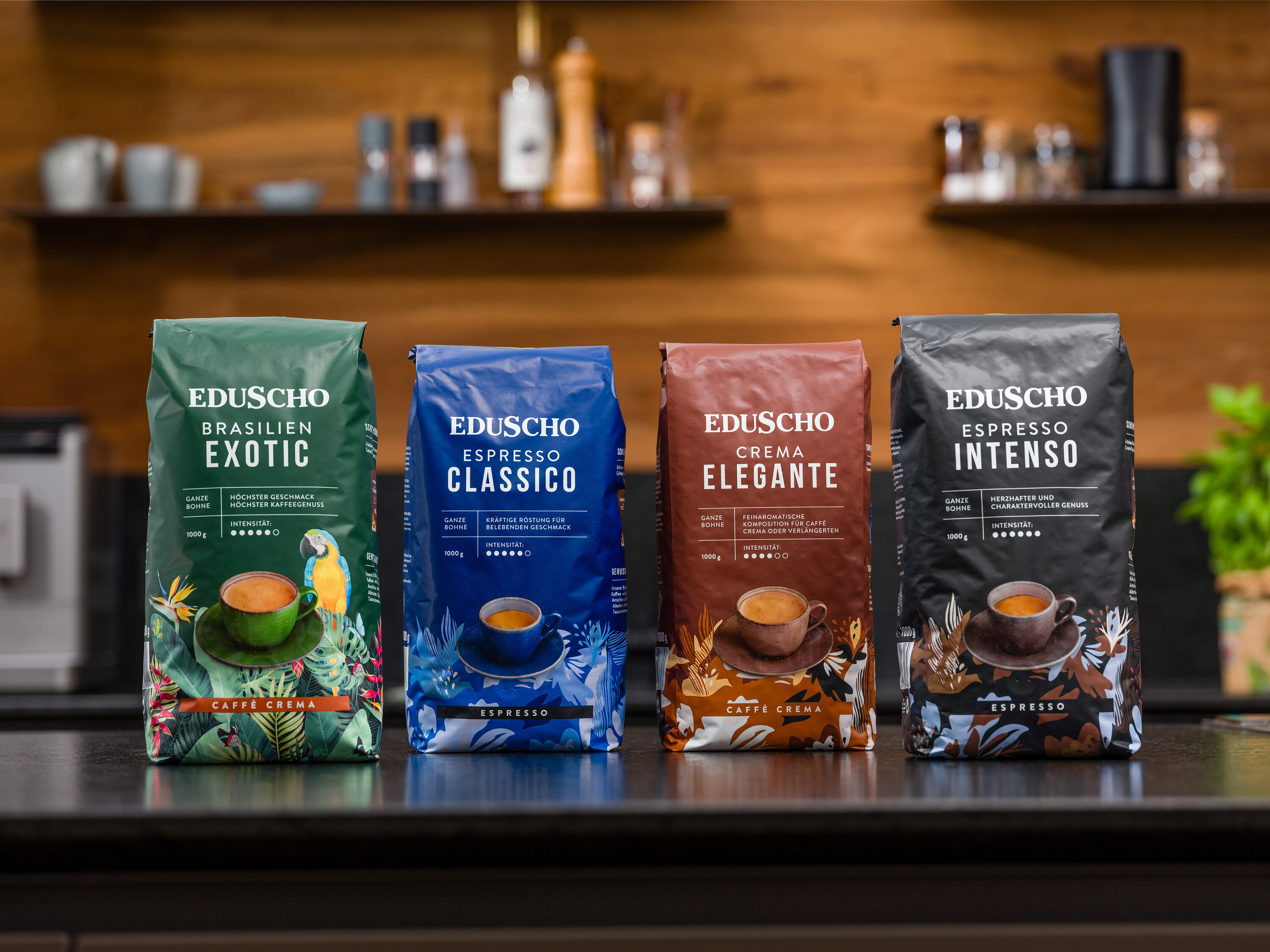 Vier Packungen Eduscho Kaffee verschiedener Sorten stehen auf einem Tisch vor einer Küchenzeile.