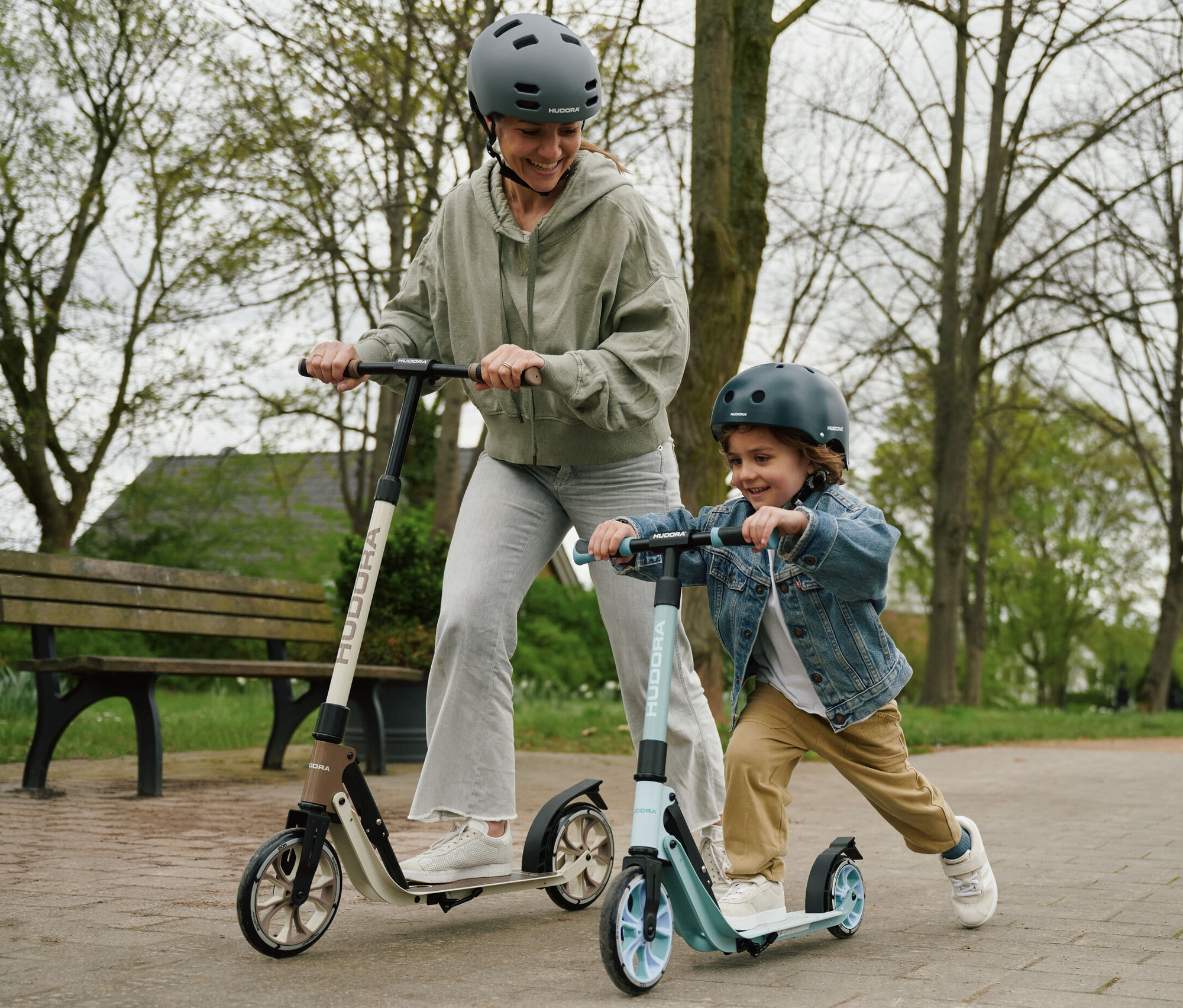 Eine Frau und ein Kind fahren mit HUDORA BigWheel 180 Advanced Junior Rollern im Park.
