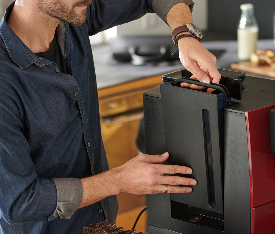 Mann füllt Wasser in einen roten Tchibo Office Kaffeevollautomaten.