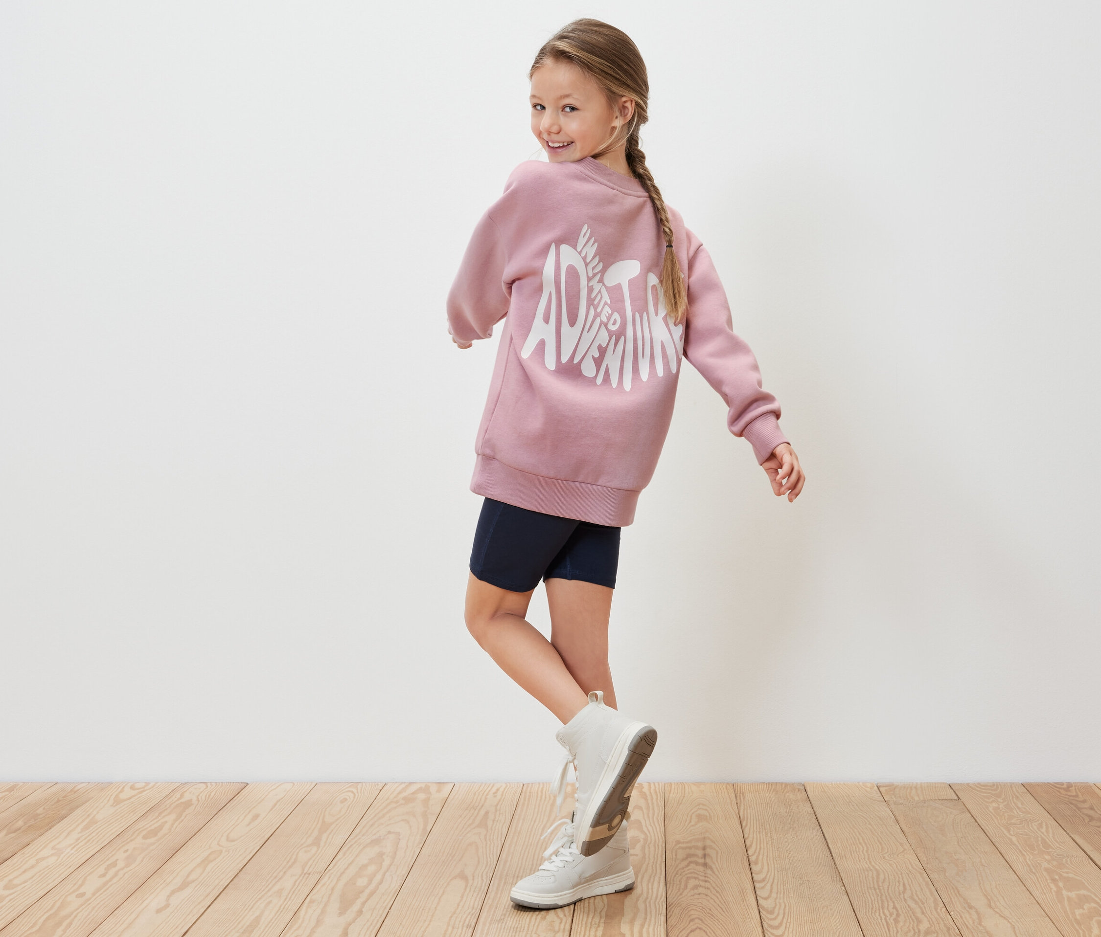 Mädchen blickt über die Schulter, trägt ein rosa Kinder-Sweatshirt.