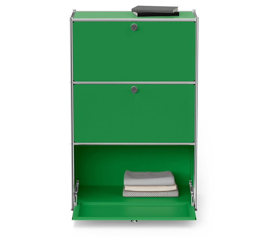 Ein grüner Schrank mit drei Fächern, die oberen zwei sind geschlossen, auf dem oberen Fach liegt ein Buch, das untere Fach ist geöffnet und enthält gefaltete Handtücher.