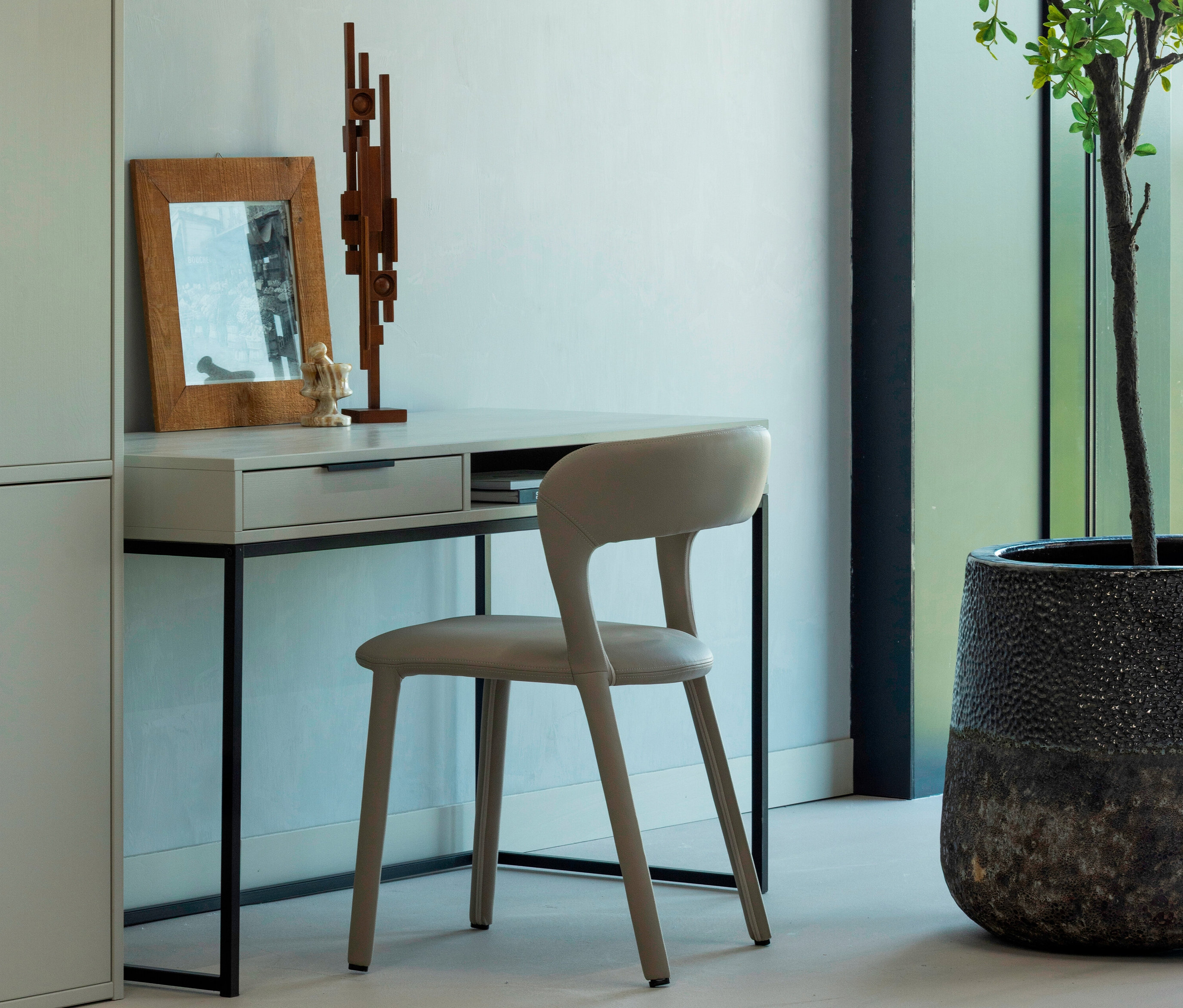 Abbildung eines WOOOD Schreibtischs »Nore« mit Stuhl, einer Skulptur und einem Bilderrahmen auf dem Tisch.