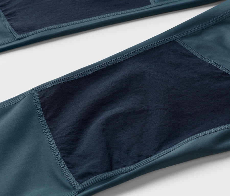 Detailaufnahme einer dunkelblau-grünen Hose mit marineblauen Stoffeinsätzen an den Knien.