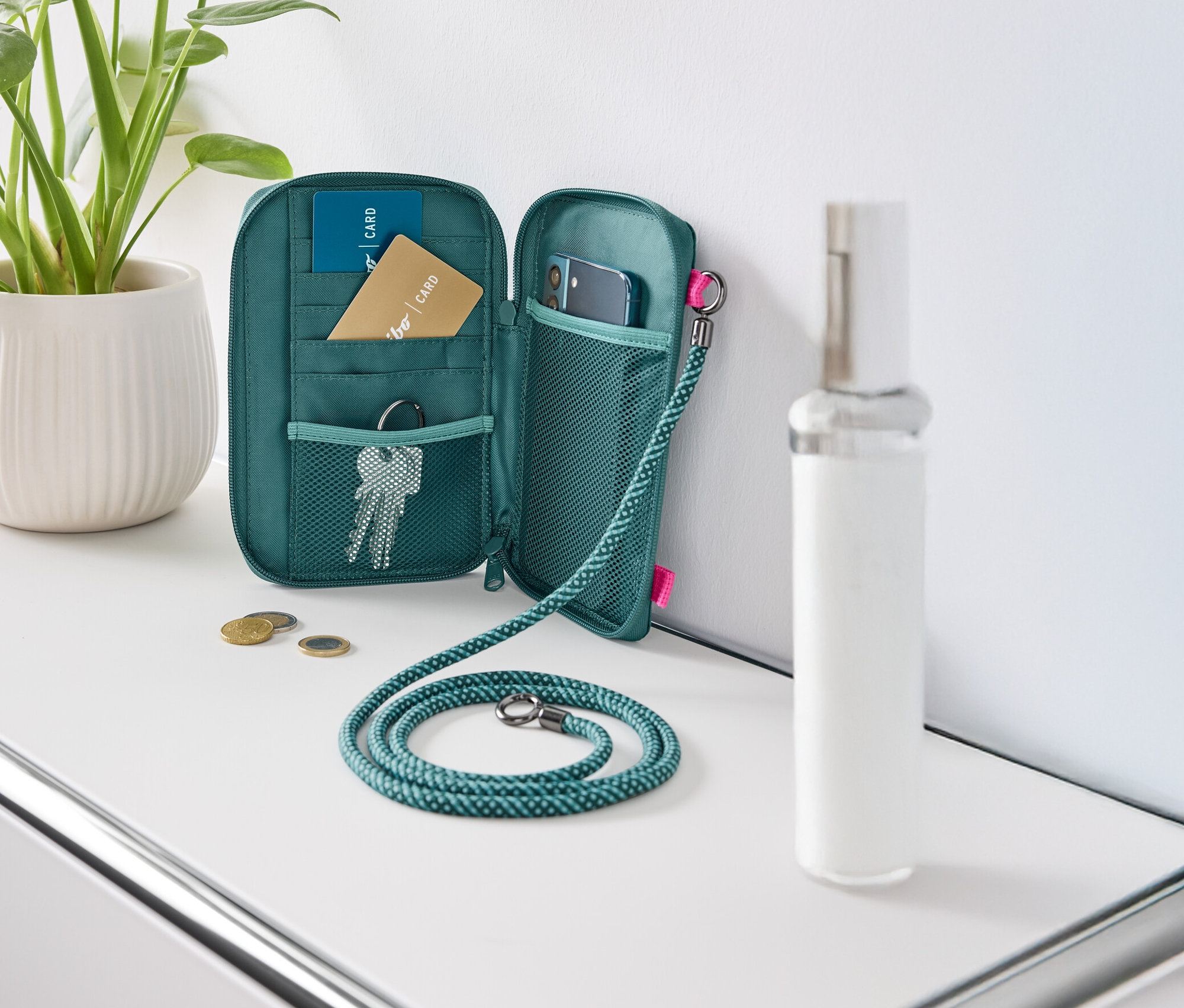 Eine grüne Geldbörse liegt offen auf einem weißen Tisch, gefüllt mit Karten, Schlüsseln und einem Handy.