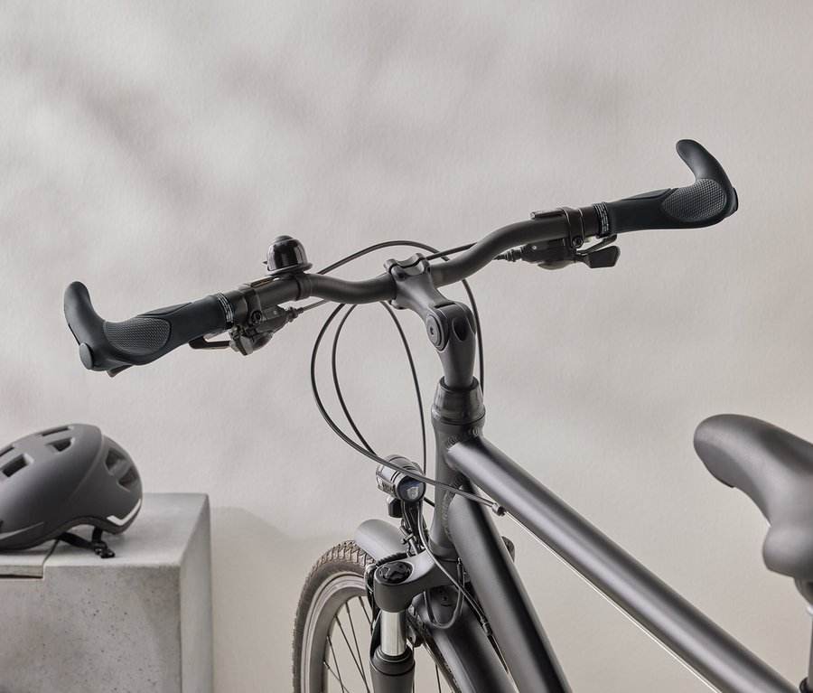 Nahaufnahme eines mattschwarzen Fahrrads mit einem schwarzen Helm auf einer Betonoberfläche im Hintergrund.