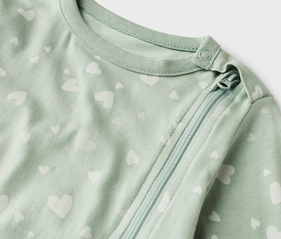 Nahaufnahme eines hellgrünen Baby-Schlafanzugs mit weißem Herzmuster und Reißverschluss.