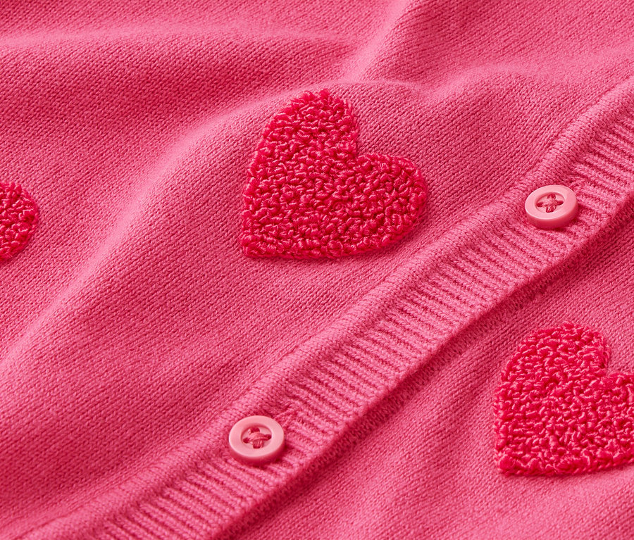 Nahaufnahme einer pinkfarbenen Strickjacke mit Herzapplikationen und Knöpfen.