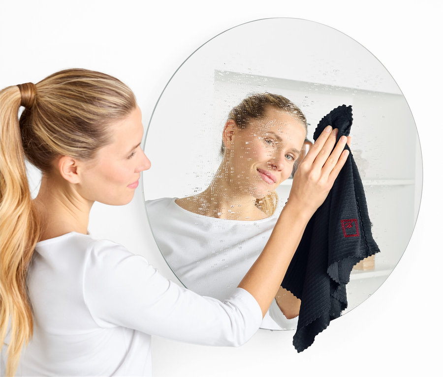 Frau putzt einen runden Spiegel mit einem schwarzen Tuch.