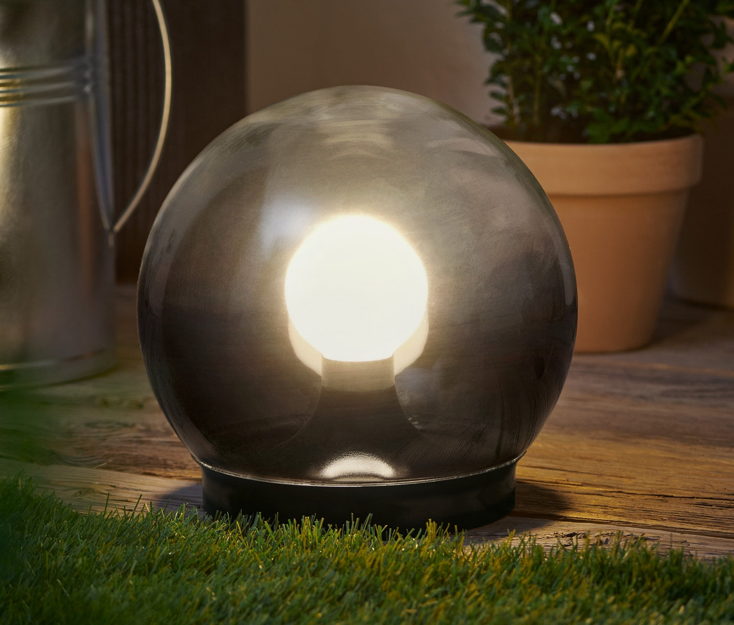 Eine Rauchglas-Kugelleuchte steht auf einer Holzoberfläche neben Pflanzen.