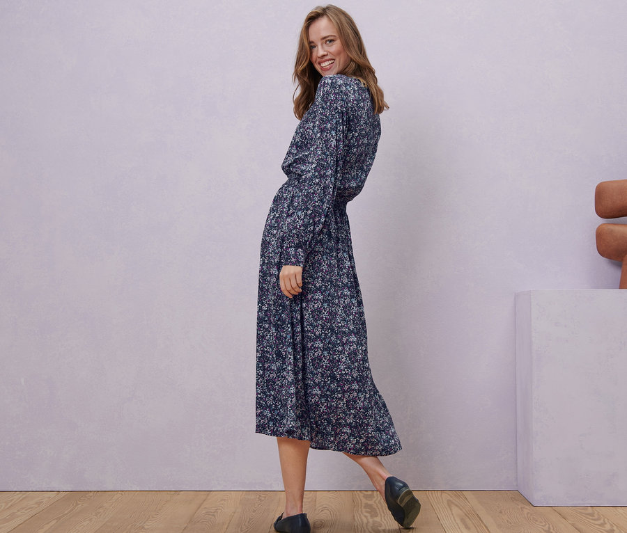 Frau lächelt über die Schulter und posiert in einem floralen Midikleid.