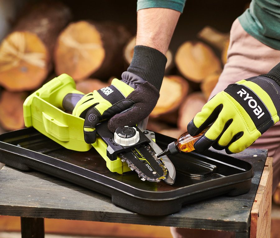Mann ölt mit Handschuhen die Kette der RYOBI 18 V One+ Brushless Akku-Einhand-Kettensäge.