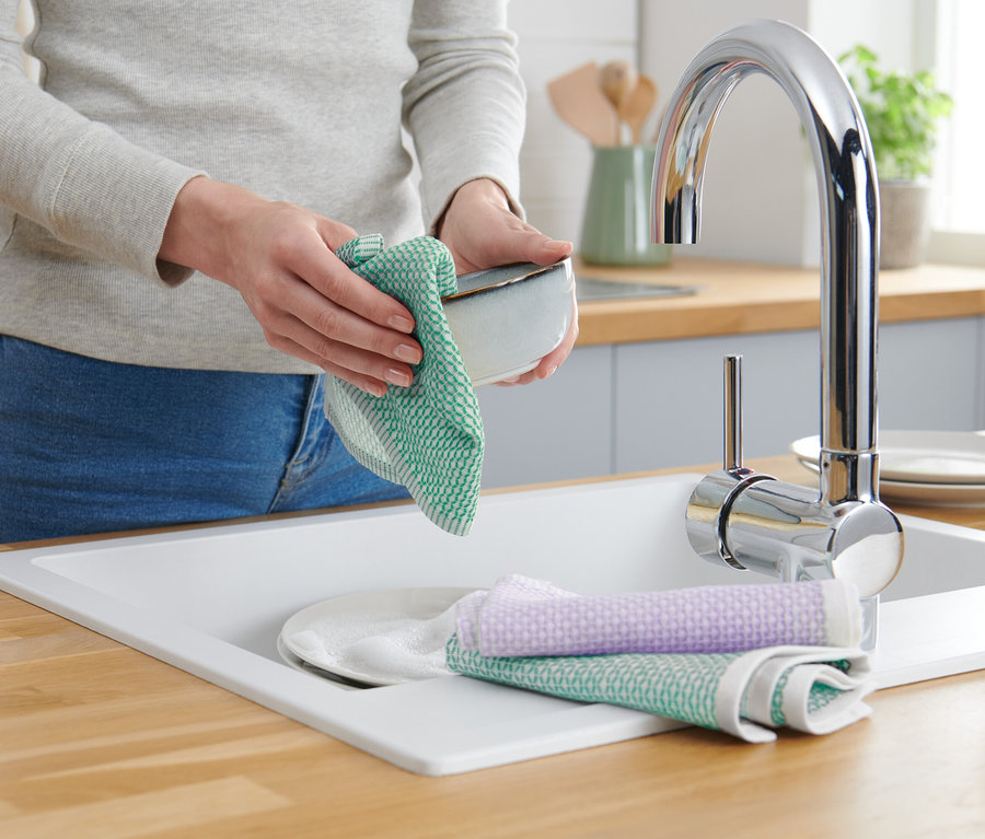 Frau trocknet Schüssel mit grünem Geschirrtuch an Spüle mit Armatur und Seifenspender.