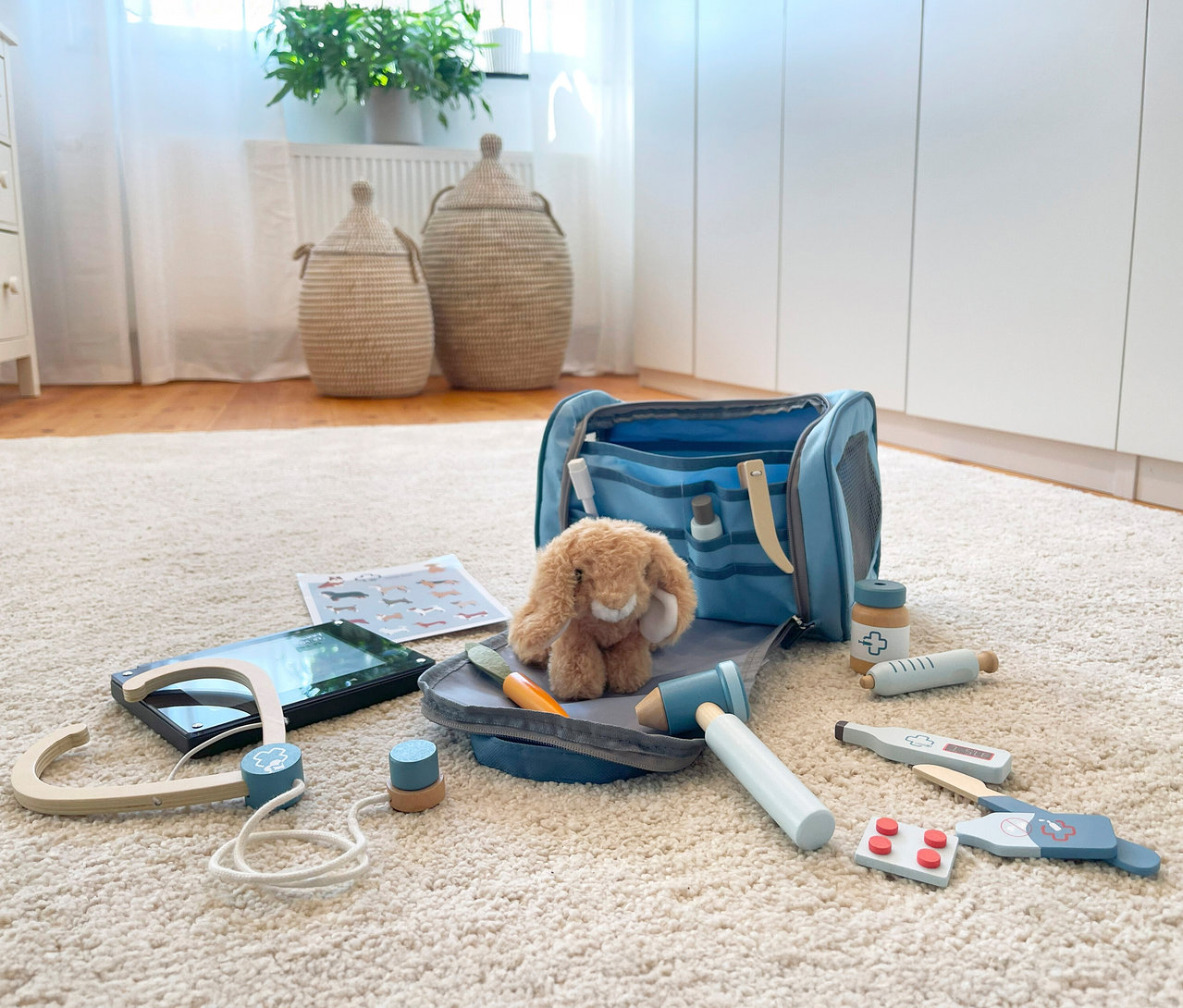 Auf einem Teppich liegt eine geöffnete blaue Tierarzttasche von Small Foot mit einem Plüschhasen und Holzspielzeug.