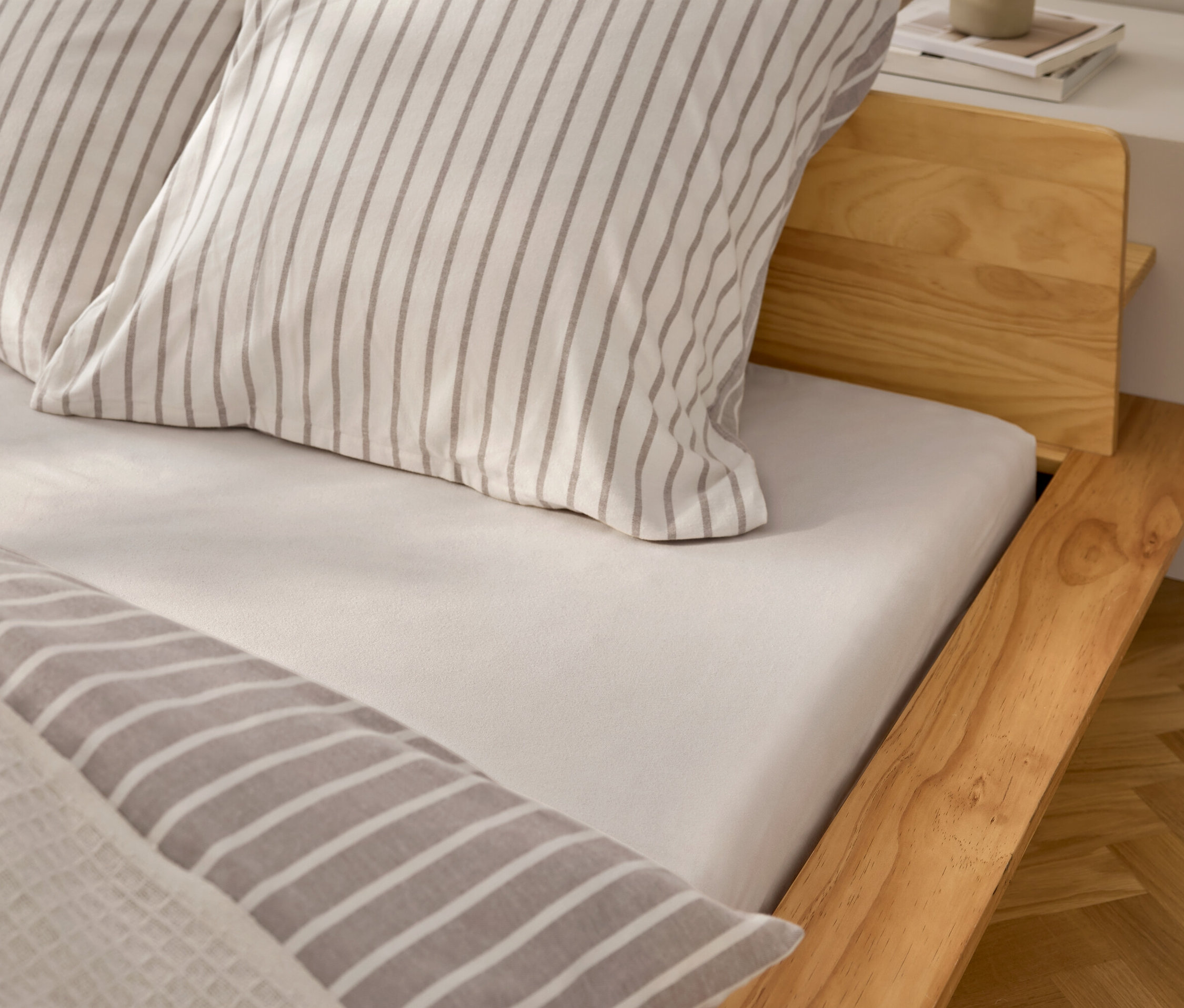 Detailansicht eines Bettes mit weißem Spannbettlaken und Kissen mit grauen Streifen.