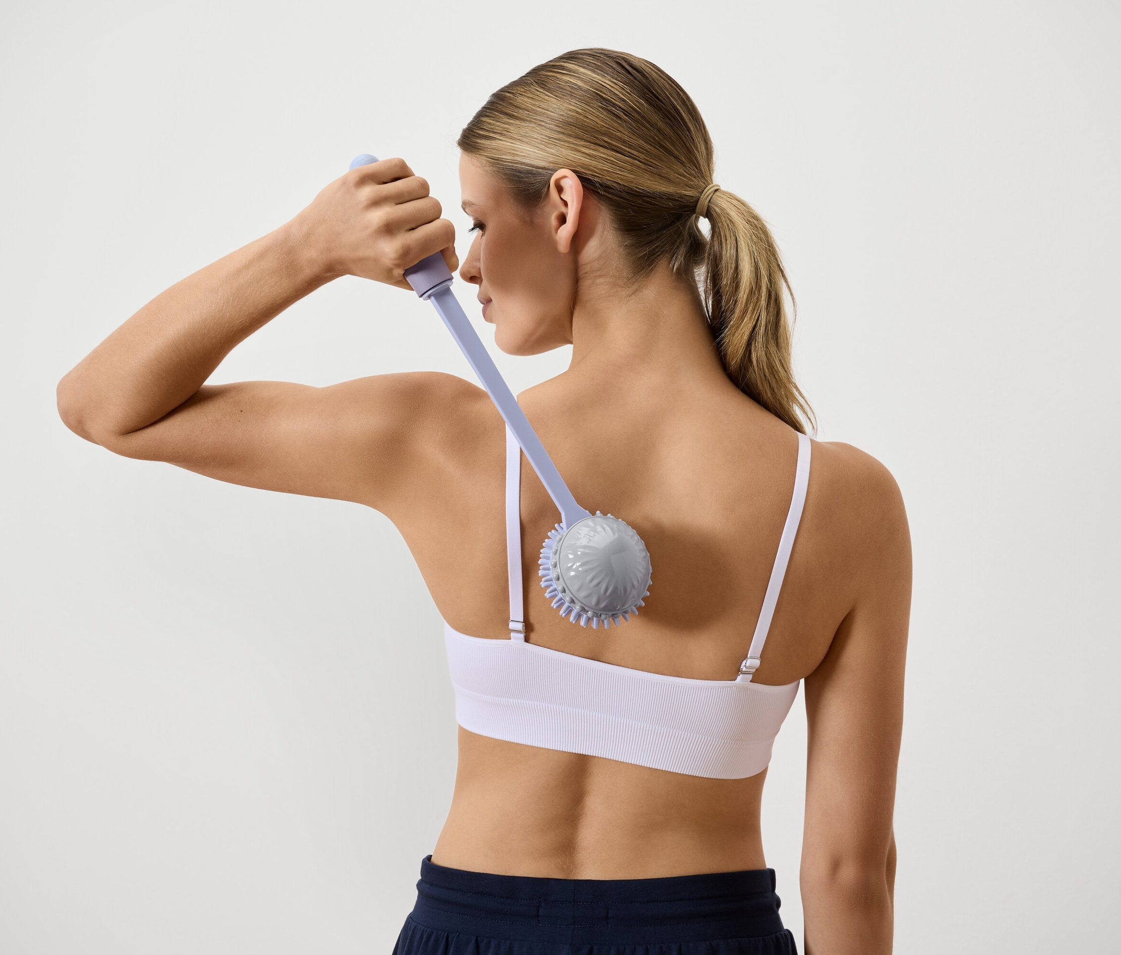 Rückansicht einer Frau, die ihren Rücken mit einem Massagegerät mit langem Griff massiert.