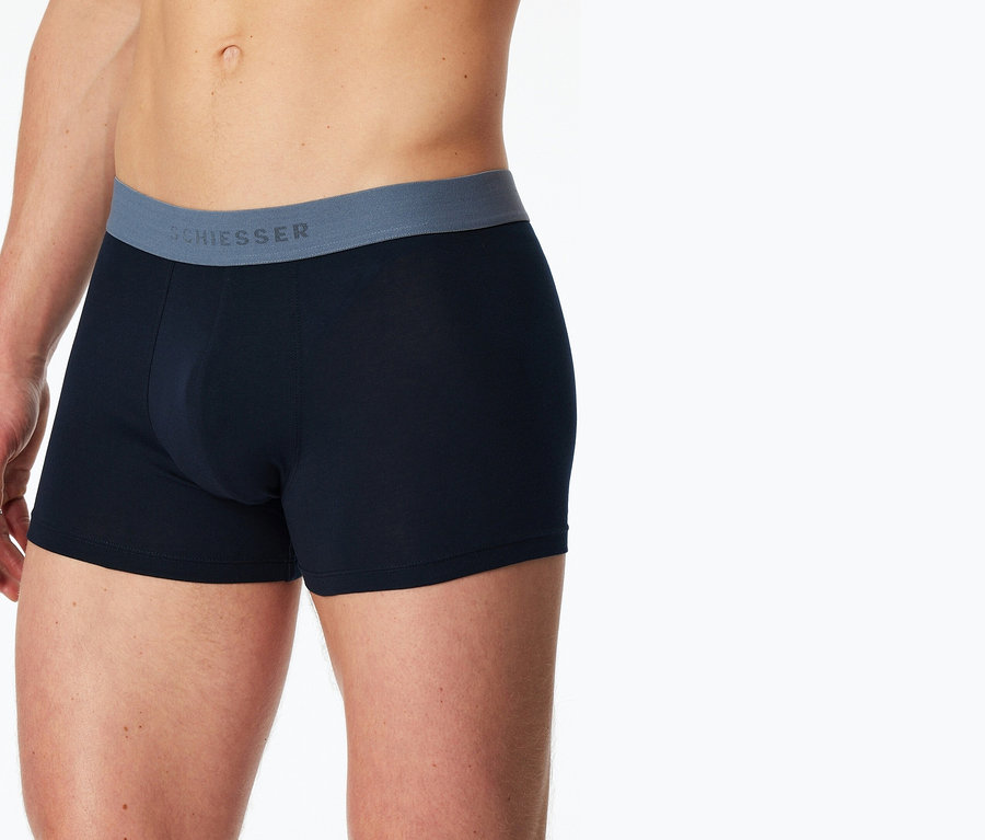 Mann trägt blaue Boxershorts mit grauem Bund mit dem Schriftzug 'SCHIESSER'.