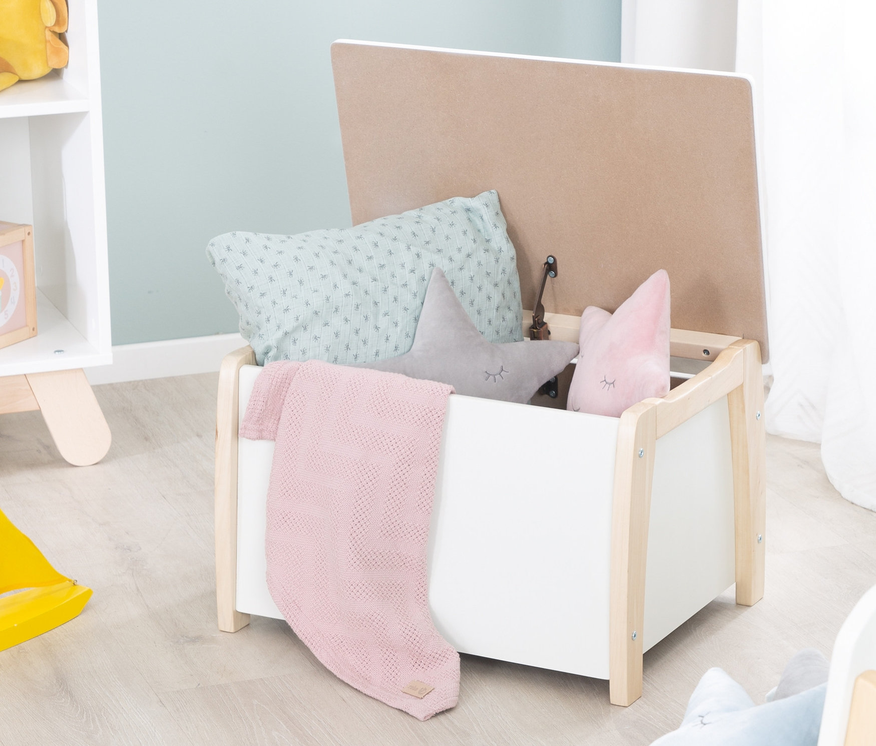 Offene roba Spielzeugtruhe mit Kissen und Decke darin.