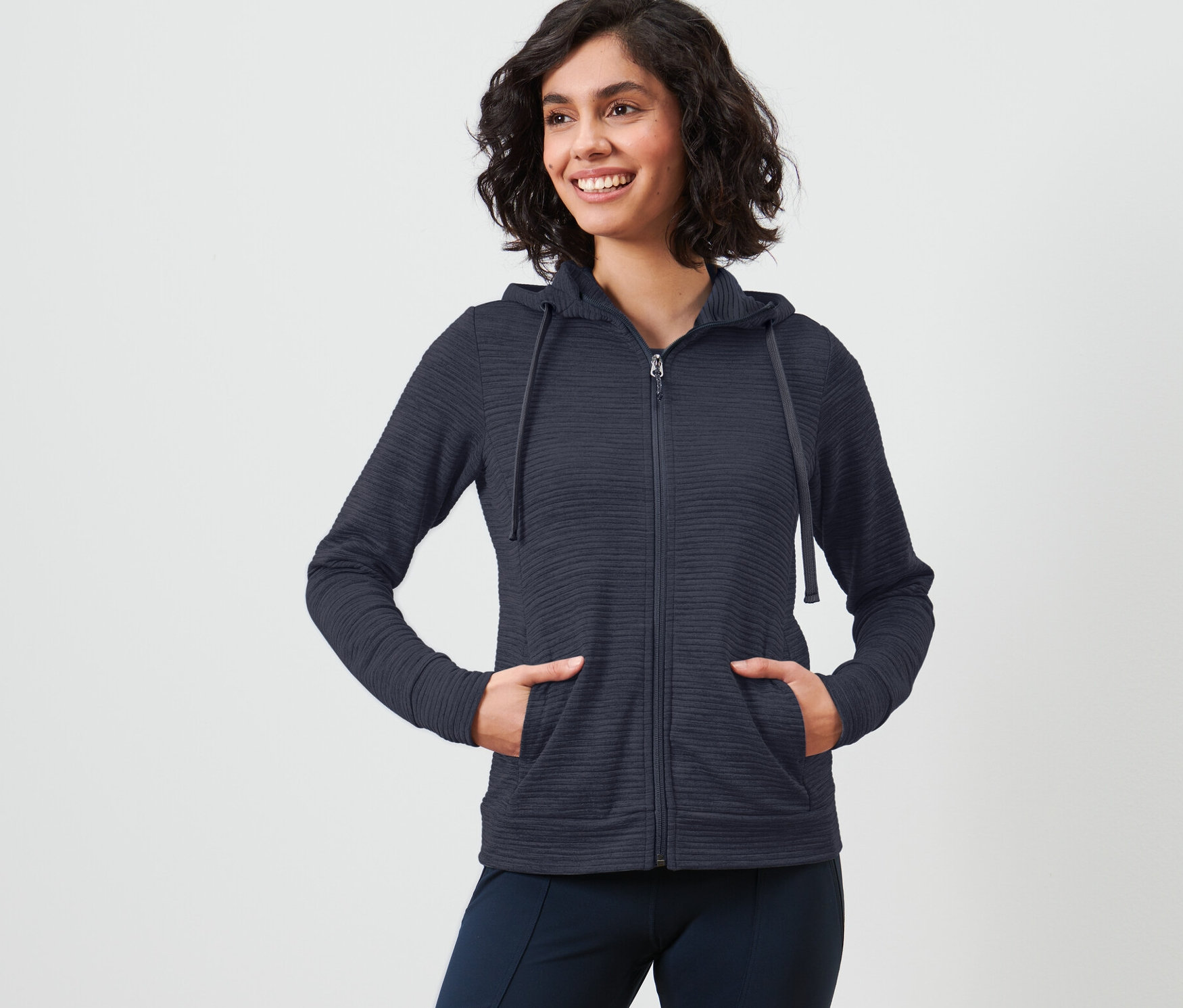 Frau mit kurzen Haaren posiert in blauer Kapuzenjacke.