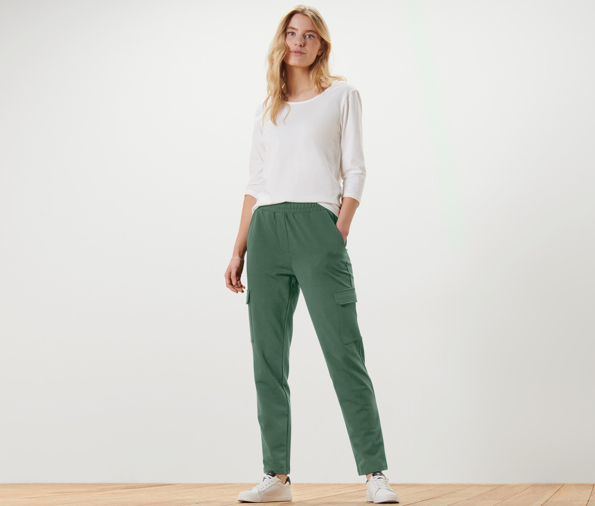 Frau posiert in grünen Joggpants mit Cargo-Taschen und weißem Shirt.