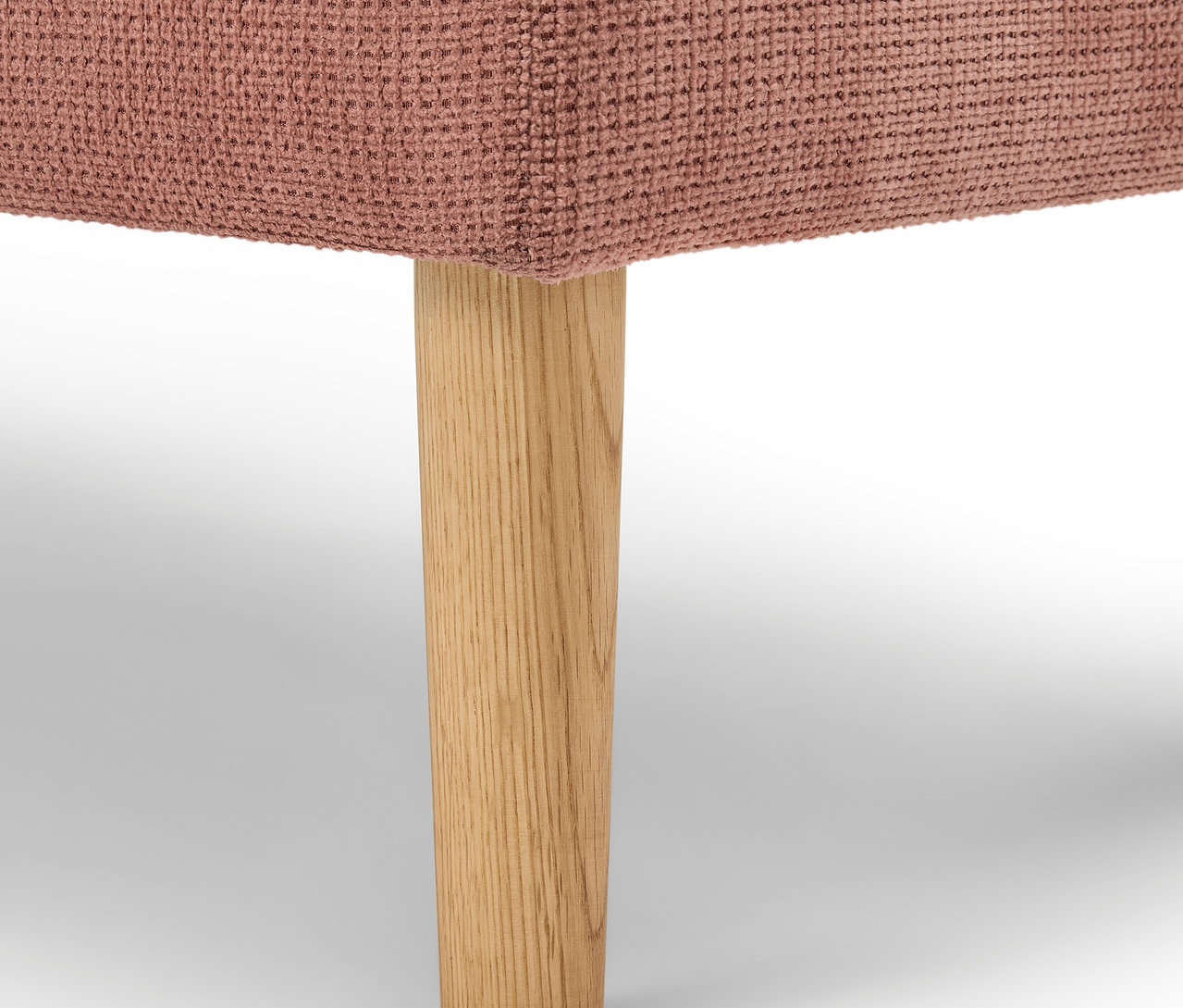 Detail eines rosafarbenen Polstermöbels mit Holzbein.