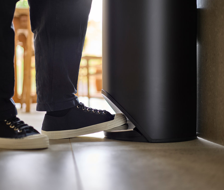 Ein Fuß in einem Turnschuh tritt auf das Pedal eines schwarzen Mülleimers.