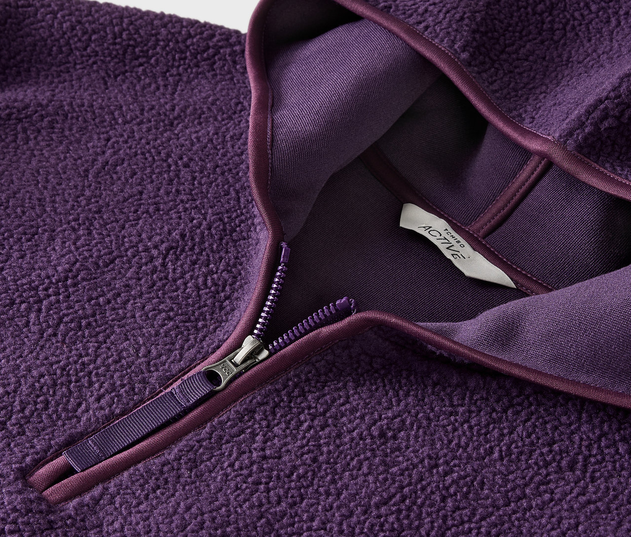 Detailansicht eines lila Fleece-Pullovers mit Reißverschluss und Etikett.