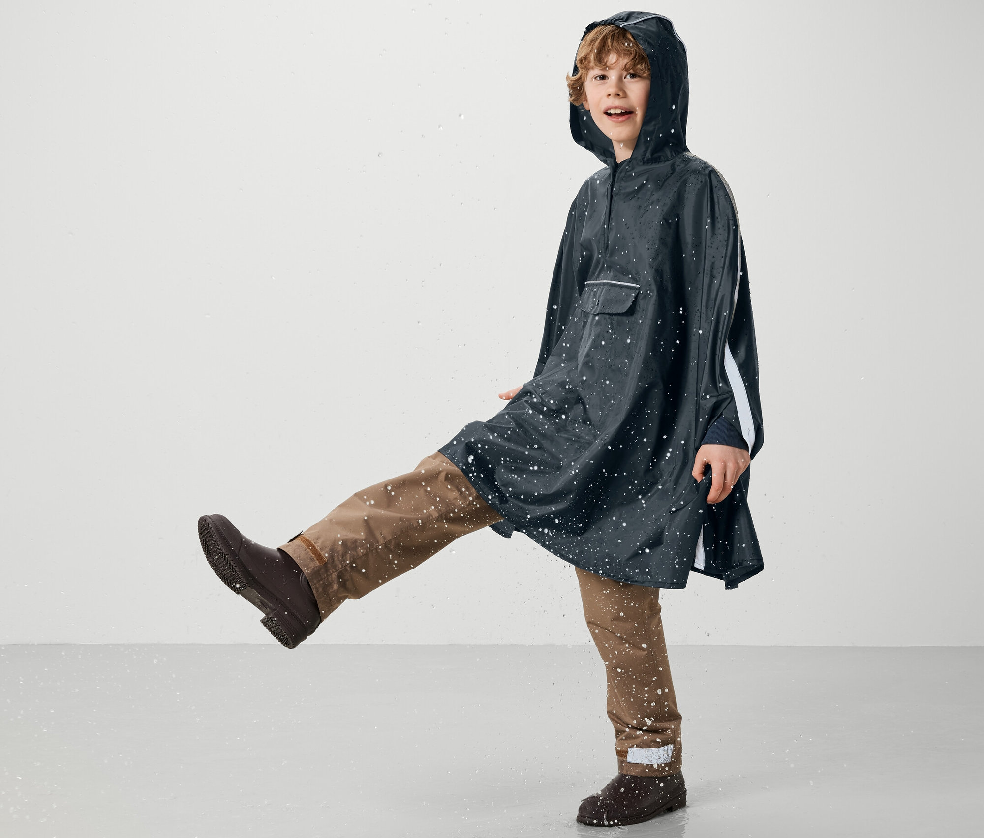 Junge im blauen Kinder-Regenponcho tritt in Wasser.